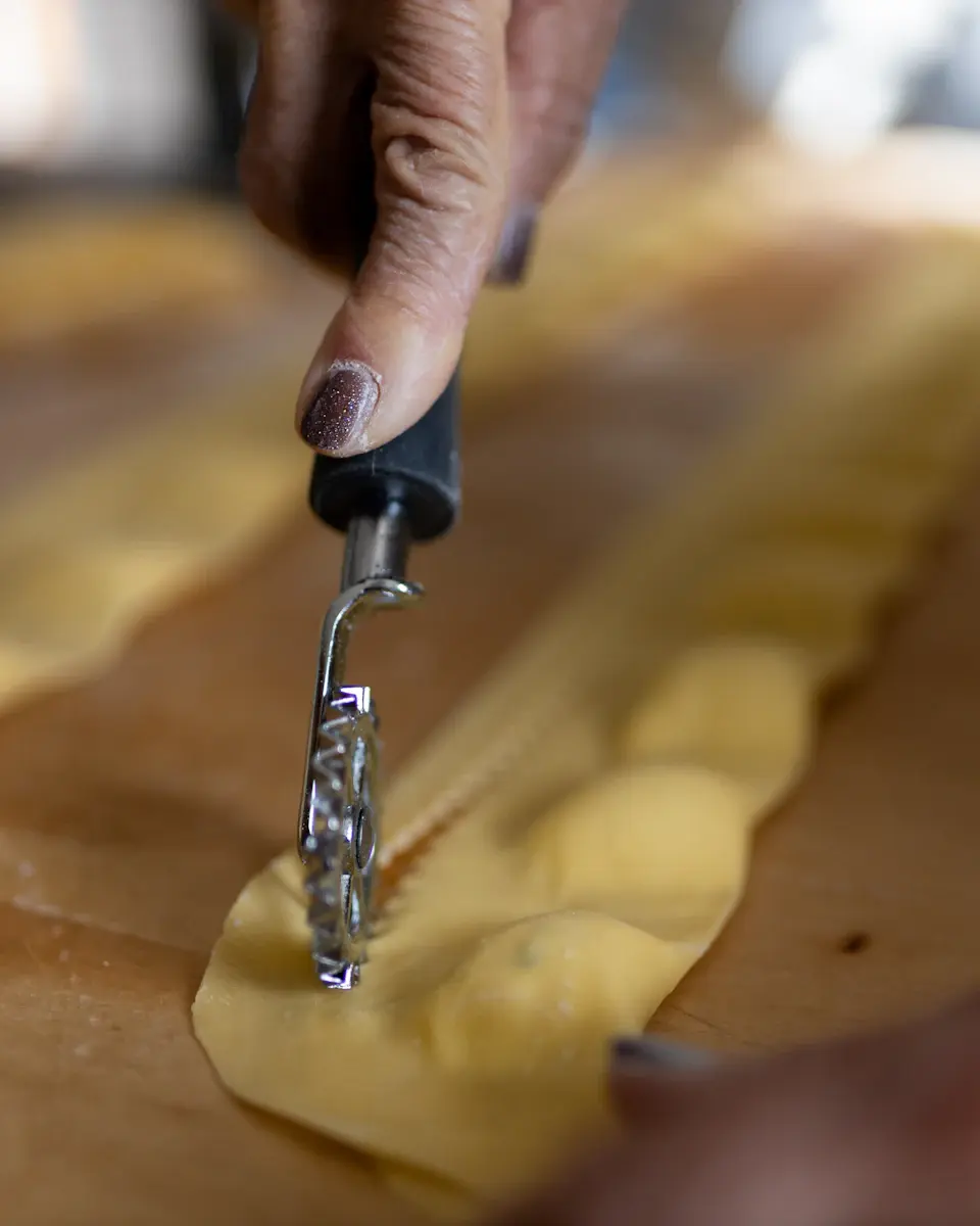 Una mano che taglia ravioli freschi con una rotella dentellata su un tagliere di legno