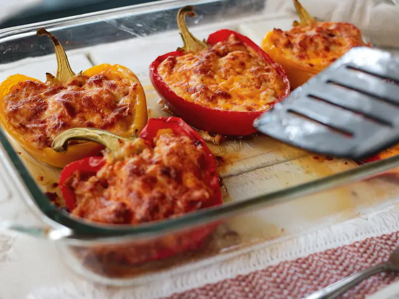 Peperoni rossi e gialli ripieni, coperti di formaggio fuso e dorato, in una pirofila di vetro